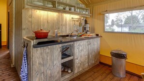 A compact kitchen with wooden cabinetry, a sink, and a window providing a view of the outside. - Tent Lodge With Sanitary Facilities at the Bedafse Bergen - Campsite (Uden)