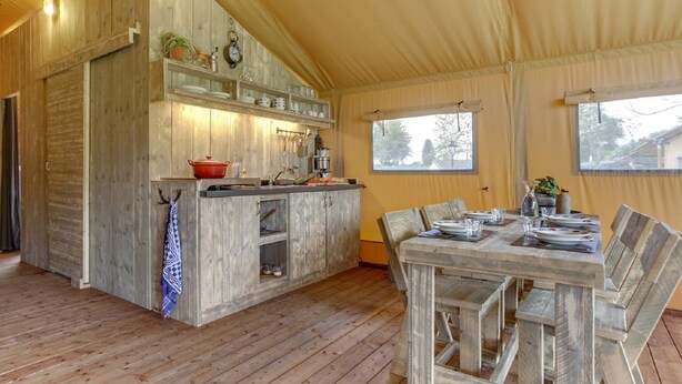 A rustic wooden interior with a dining area, kitchen, and large windows. - Tent Lodge With Sanitary Facilities at the Bedafse Bergen - Campsite (Uden)