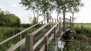 Un ponte di legno con ringhiera, immerso nel verde e attraversato da un corso d'acqua.