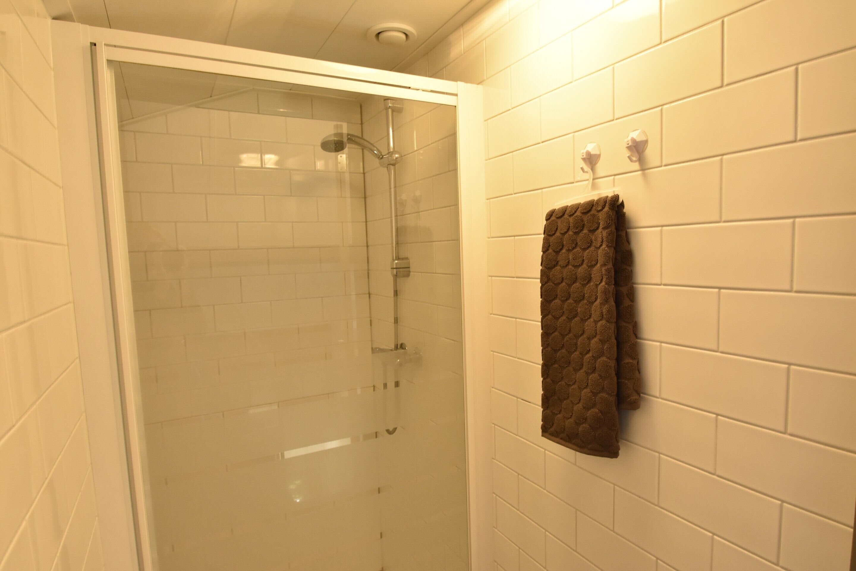 A glass-enclosed shower with white tiles and a towel hanging on the wall.