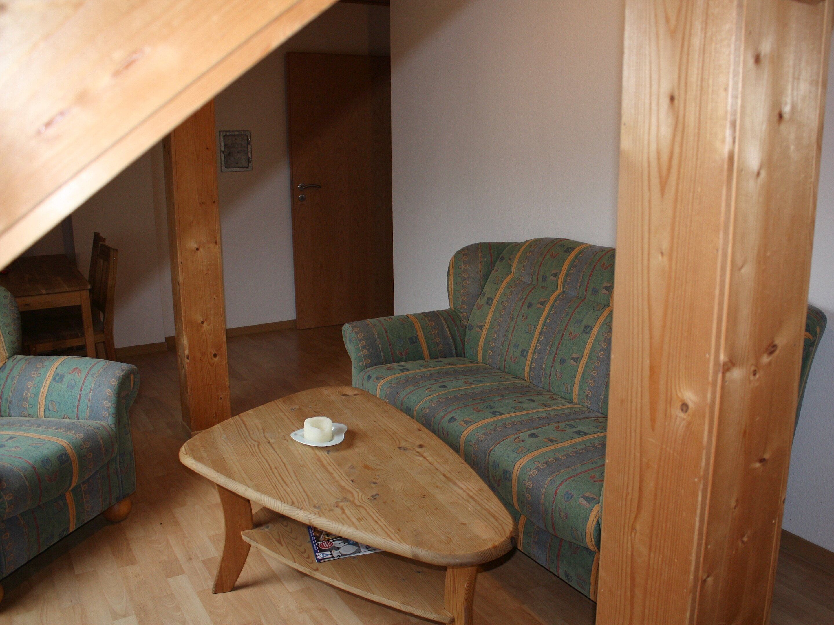 Una habitación acogedora con techo de madera, un sofá verde, un sillón a juego y una pequeña mesa de madera con una taza.