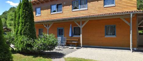 A two-story wooden house with a covered patio, a gravel driveway, and a small garden area.