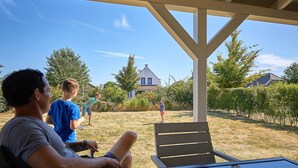 Un espacio al aire libre cubierto con una mesa y sillas, un jardín con césped y una casa al fondo.