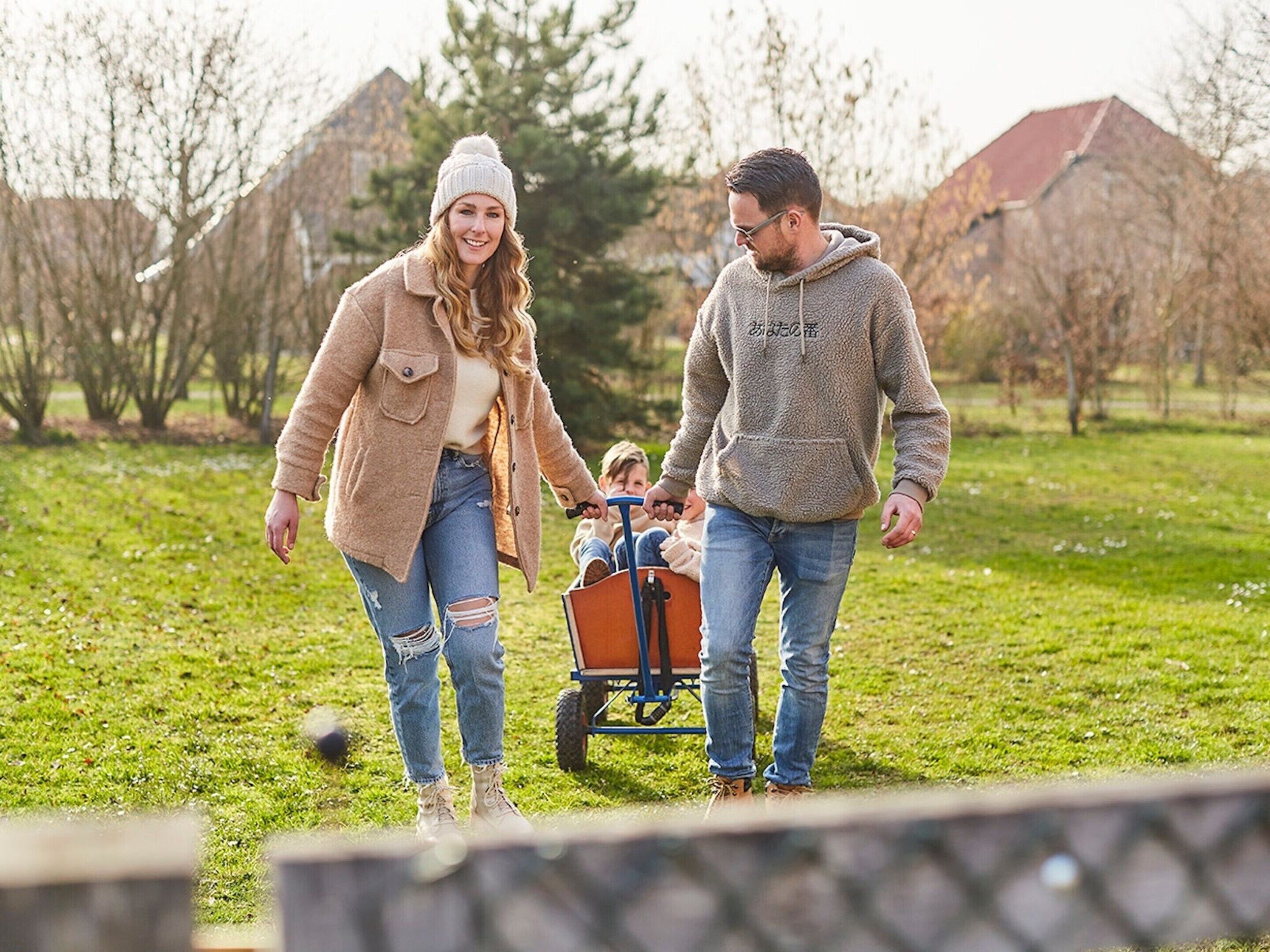 A family walking in a park with a child in a wagon.