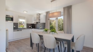 A modern kitchen with white cabinets, a built-in oven, and a dining area with a table and chairs. - Comfortable Villa With Combi-microwave, Near the Beach (Kamperland)