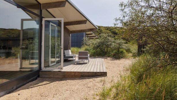 Eine moderne Außenterrasse mit Glastüren, die zu einem Sitzbereich führen, umgeben von natürlicher Bepflanzung.