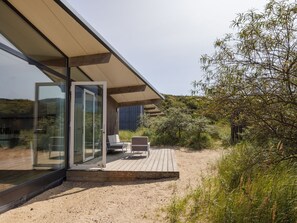 Una terraza moderna al aire libre con puertas de cristal que dan a un área de estar, rodeada de vegetación natural.