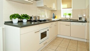 A modern kitchen with white cabinets, a stove, an oven, and a coffee maker. - Relaxing Nature Escape (Heel)
