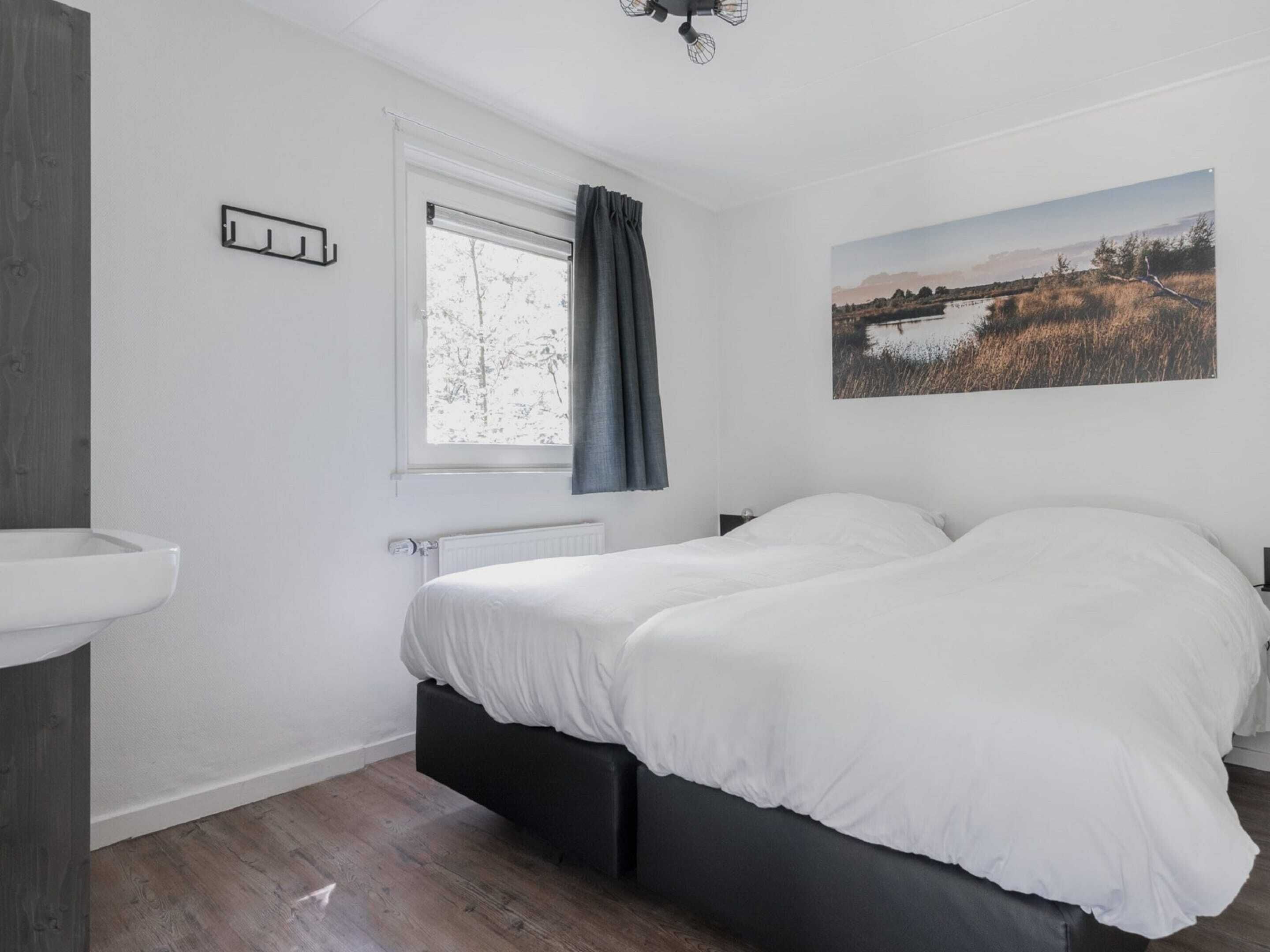 Un dormitorio con cama, una ventana con cortinas, un radiador y un cuadro colgado en la pared.