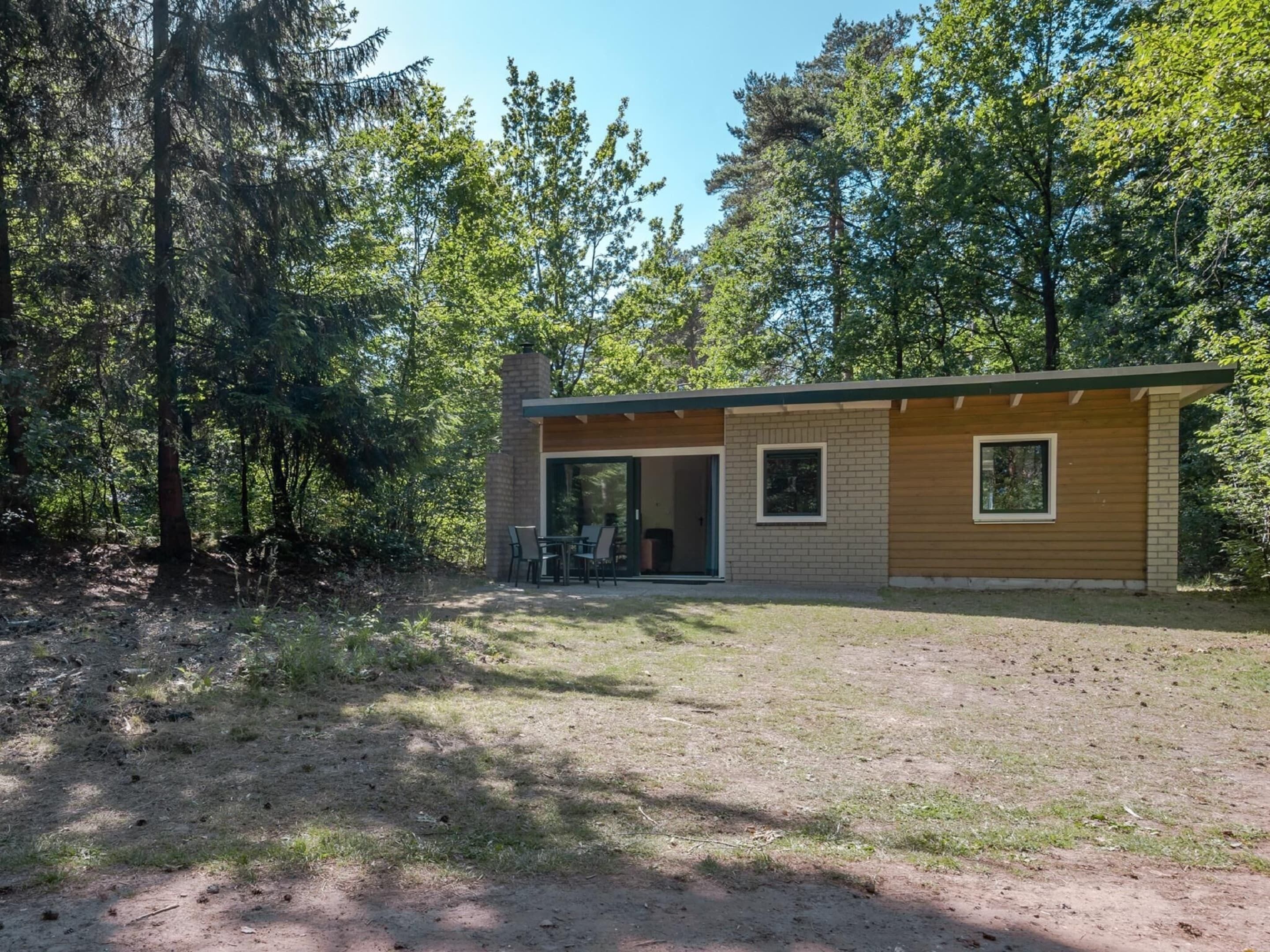 Eine moderne Hütte mit Backsteinschornstein, einer Schiebetür als Eingang und einer kleinen Terrasse mit Tisch und Stühlen.