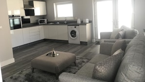 A modern kitchen with a washing machine, a microwave, and a sink. There is a grey sofa and a rug in the living area. - Appin Apartment (Inverness)