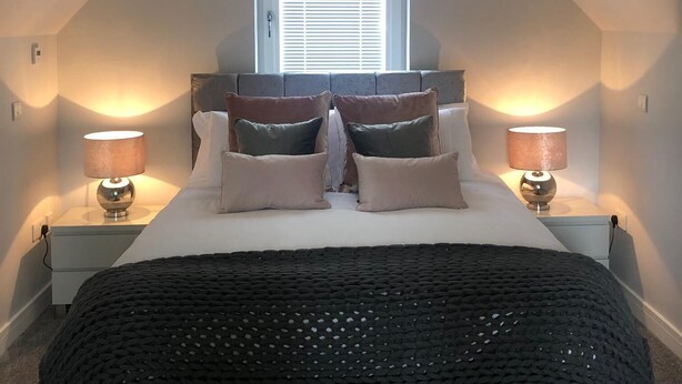 A bedroom with a bed, two bedside tables with lamps, a window with blinds, and a sloped ceiling. - Appin Apartment (Inverness)