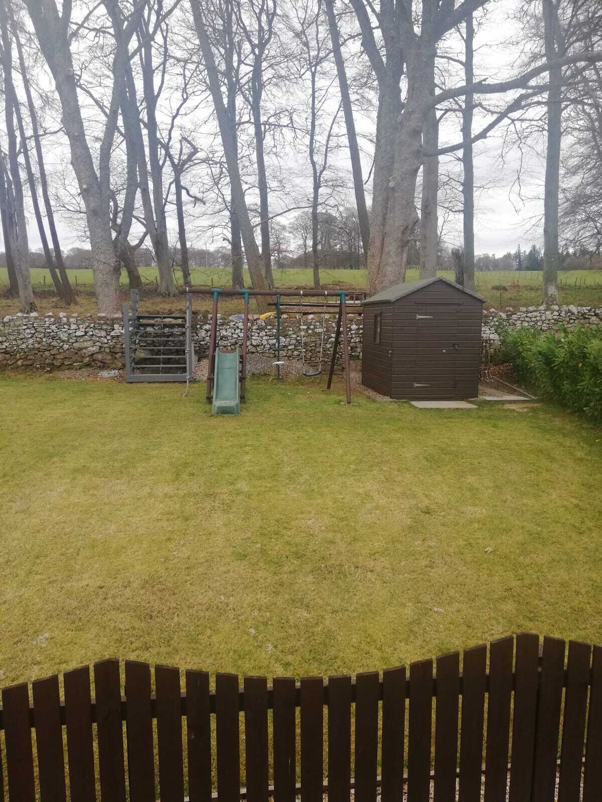 A grassy yard with a swing set, a small shed, and a stone wall.
