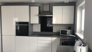 A modern kitchen with white cabinetry, a built-in oven, a microwave, and a toaster. - Appin Apartment (Inverness)