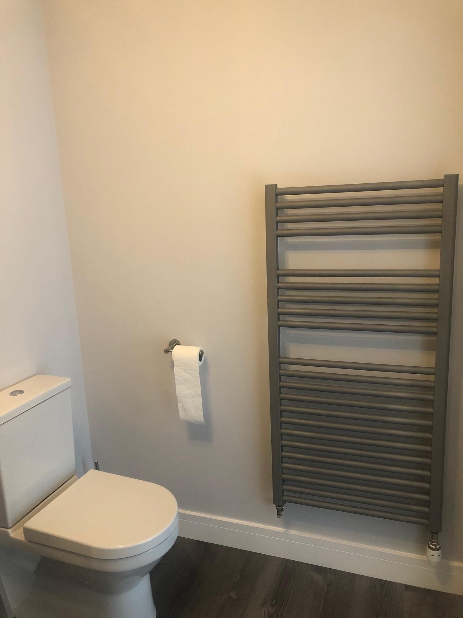 A bathroom with a toilet, a towel rack, and a wooden floor.