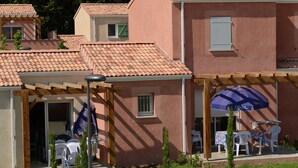 A building with a tiled roof, a covered patio with outdoor seating, and a small garden area. - Apartment in Le Paradou With Pool & Sauna (Paradou)