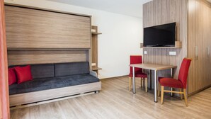 A modern room with a sofa, a TV mounted on a wooden cabinet, and a dining table with chairs. - Apartment in Kleinarl Near Ski Lift (Kleinarl)