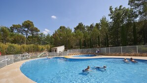 Une piscine à bord incurvé, entourée d’une clôture, avec des arbres en arrière-plan.