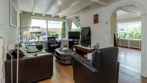 A modern living room with a fireplace, leather furniture, and a large window overlooking a garden. - Cozy Holiday Home in Noordwijkerhout near Lake (Noordwijkerhout)