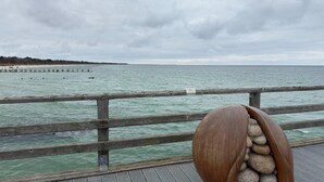 A wooden pier with a railing, a rocky structure, and a view of the sea and distant land. - Villa in Zingst Nahe Ostseestrand (Zingst)