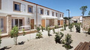 A modern building with multiple windows, a patio area with a bench, and a gravel courtyard with small plants. - Nice Apartment Near Aigues-mortes (Aigues-Mortes)