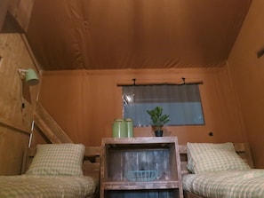 A room with two checkered upholstered chairs, a wooden table with a wire basket, a potted plant, and a window with a curtain.