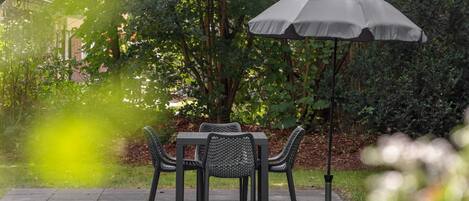An outdoor patio with a table and chairs, surrounded by greenery.