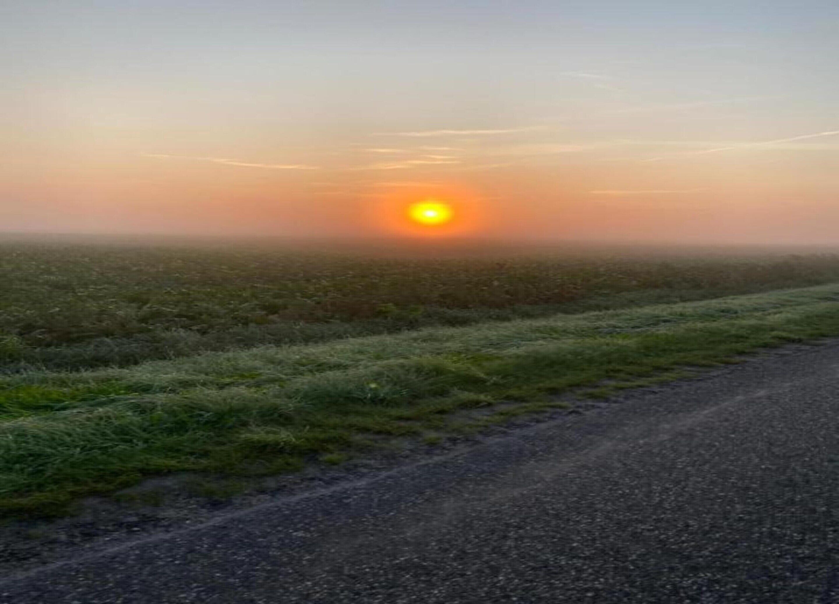 Une route de campagne avec un lever de soleil à l’horizon.