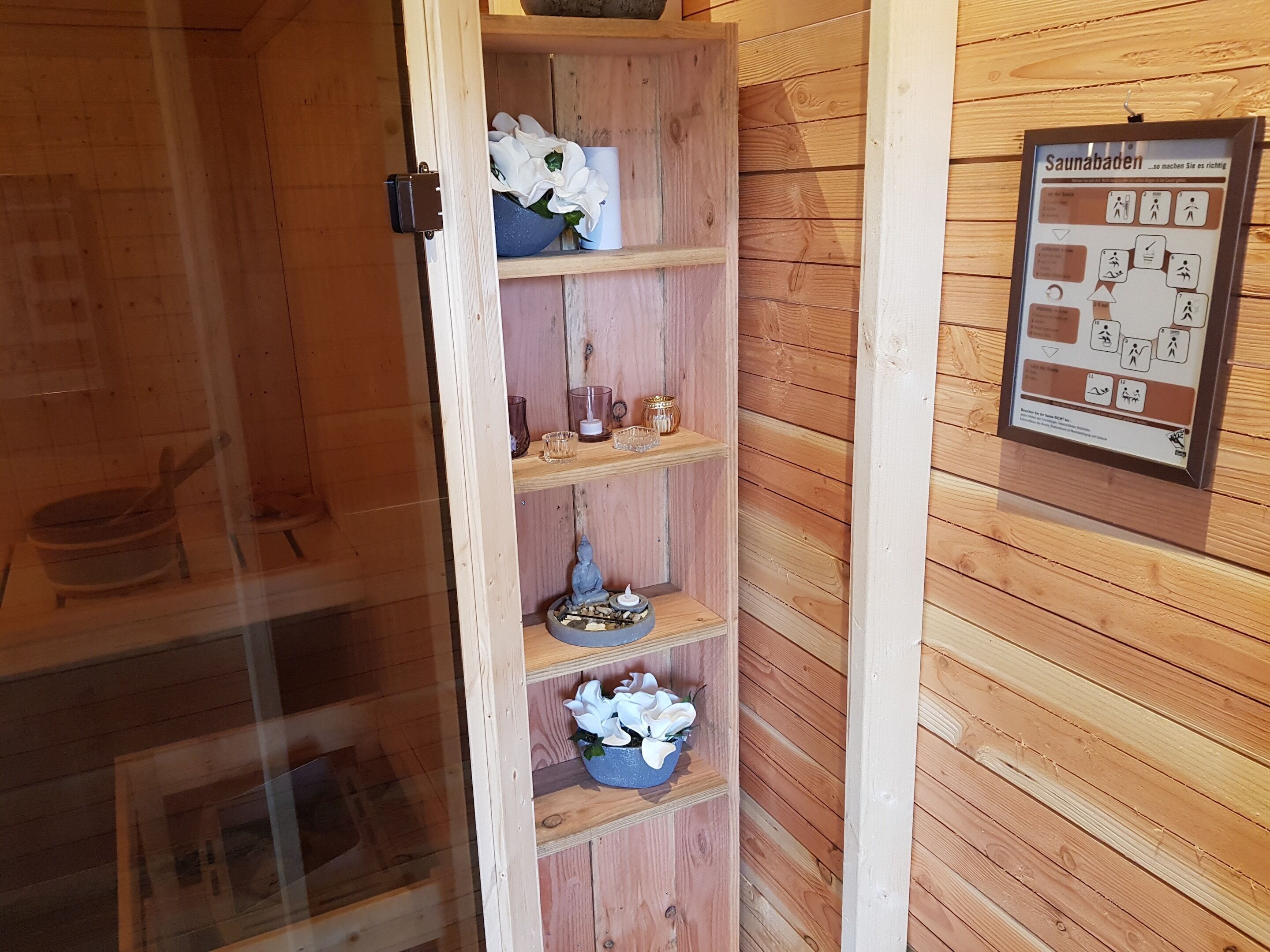 Eine Holzsauna mit Regalen, auf denen Kerzen, Blumen und eine kleine Buddha-Statue stehen.