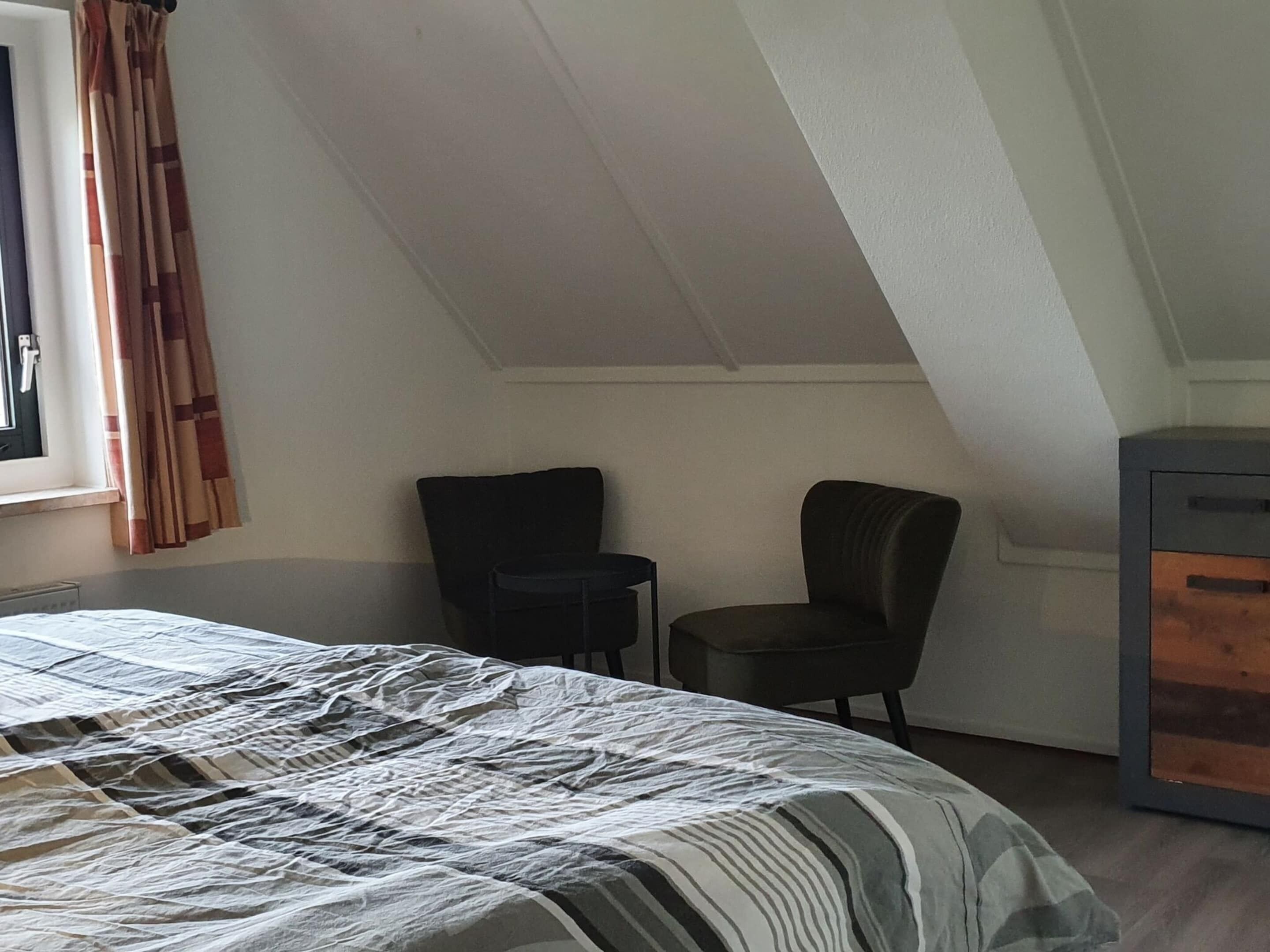 A bedroom with a bed, a chair, a small table, and a cabinet.
