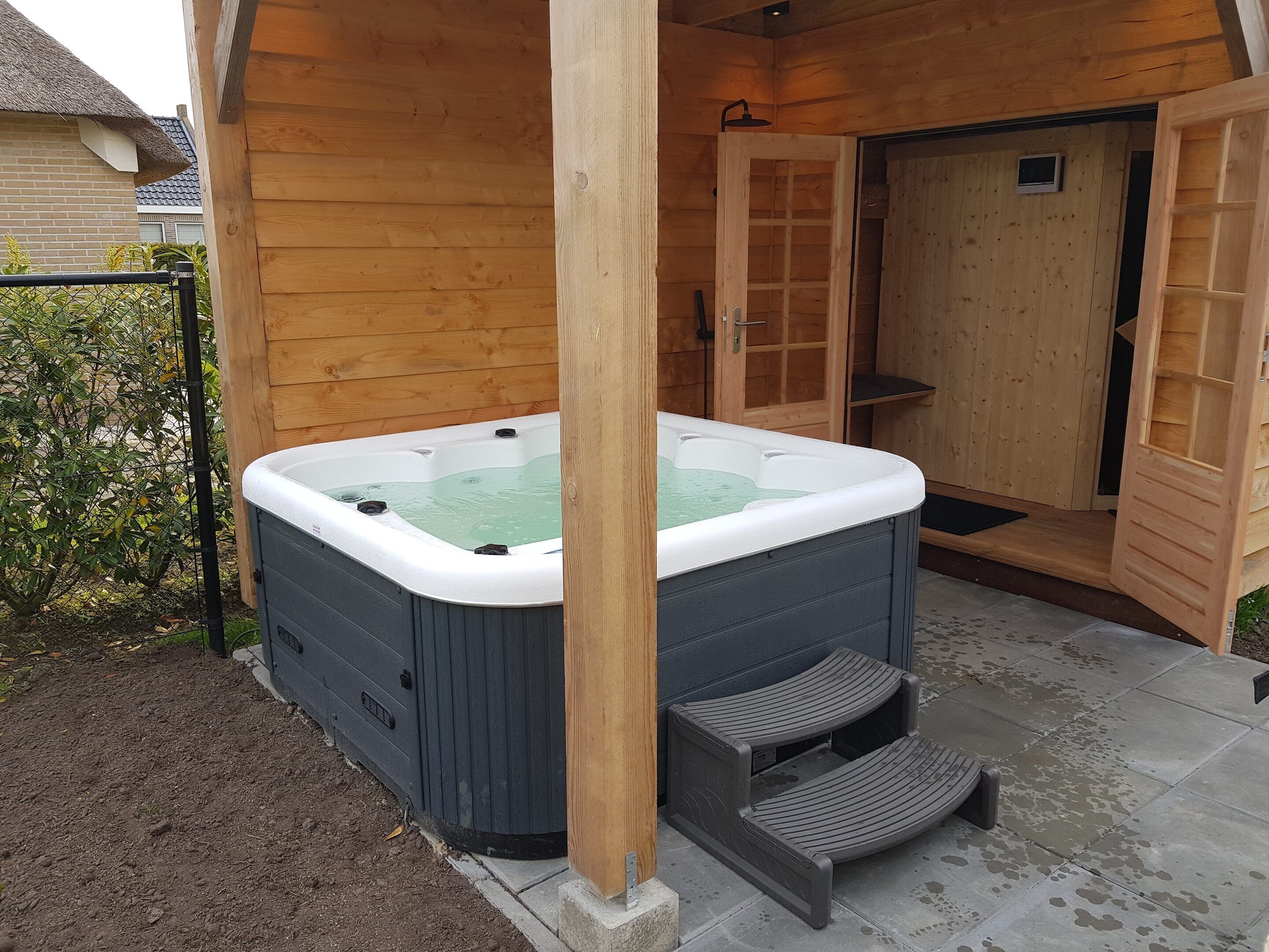 Un bain à remous avec des marches menant à l’intérieur, entouré de murs en bois et doté d’une porte.