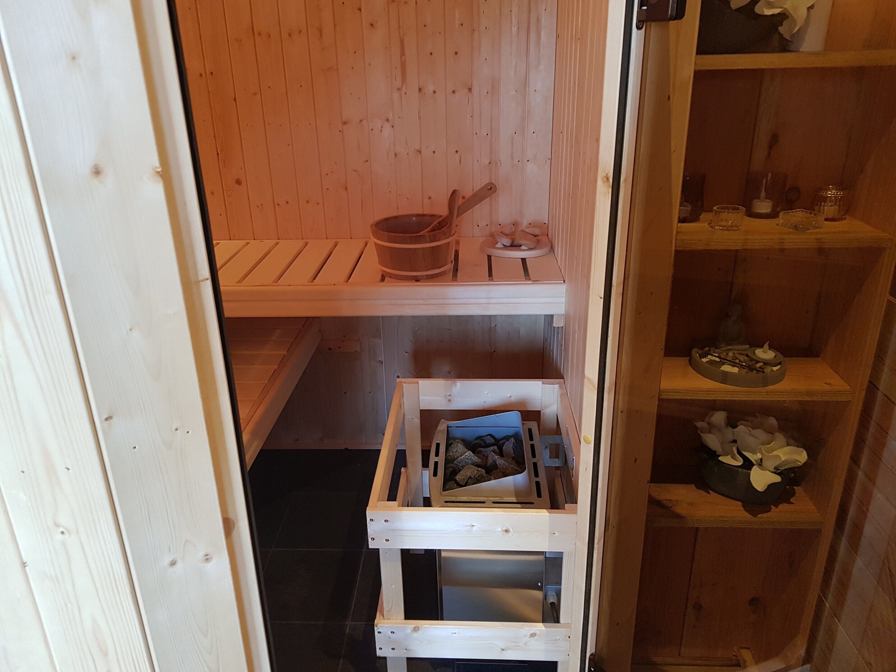 A sauna room with wooden benches, a wooden shelf with bottles, and a small table with a bowl and a candle.