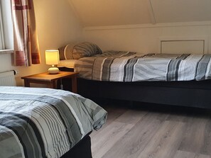 A bedroom with two beds, a bedside table with a lamp, and a radiator. - Nice Holiday Home with Sauna & Hot Tub near Wadden Sea (Tzummarum)