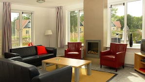 Een moderne woonkamer met een bank, fauteuils, een salontafel, een open haard en een televisie.