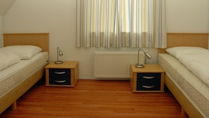 Een slaapkamer met twee eenpersoonsbedden, houten nachtkastjes en een radiator.