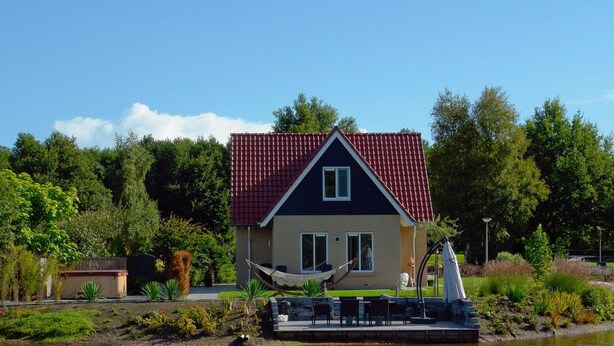 Een huis met een rood dak, een klein terras met buitenmeubilair en uitzicht op een meer.