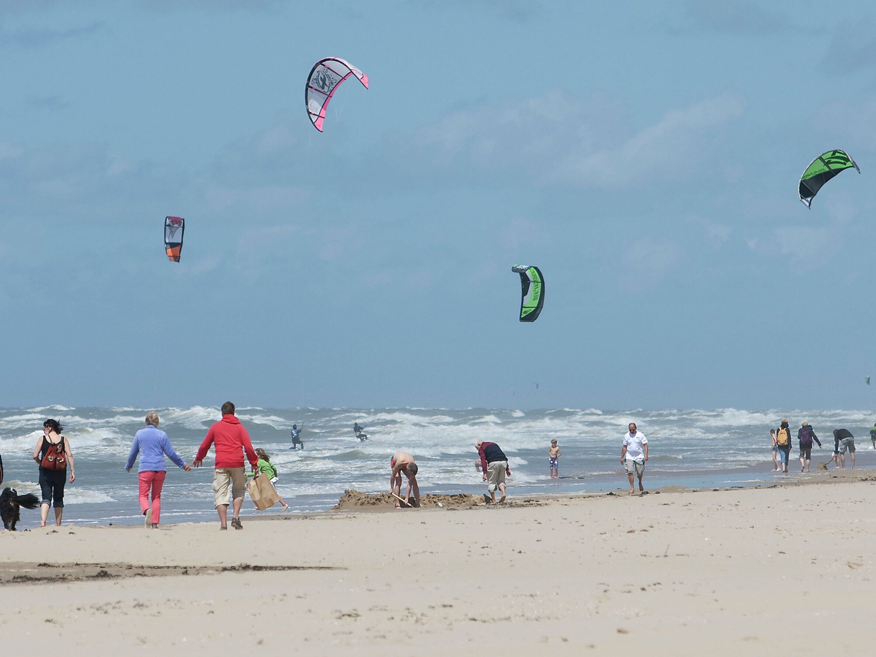 A beach with people walking and flying kites.