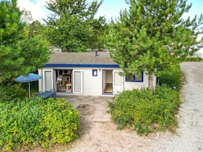 A small, single-story building with a door open to a room with a chair and table. - Cozy Chalet in the Dune Region (Egmond aan den Hoef)
