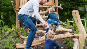 Estructura de madera para juegos en un jardín, con un hombre y dos niños jugando.