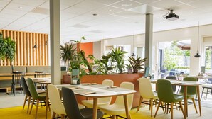 Un comedor moderno con varias mesas y sillas, un separador de madera con plantas, y un interior luminoso.