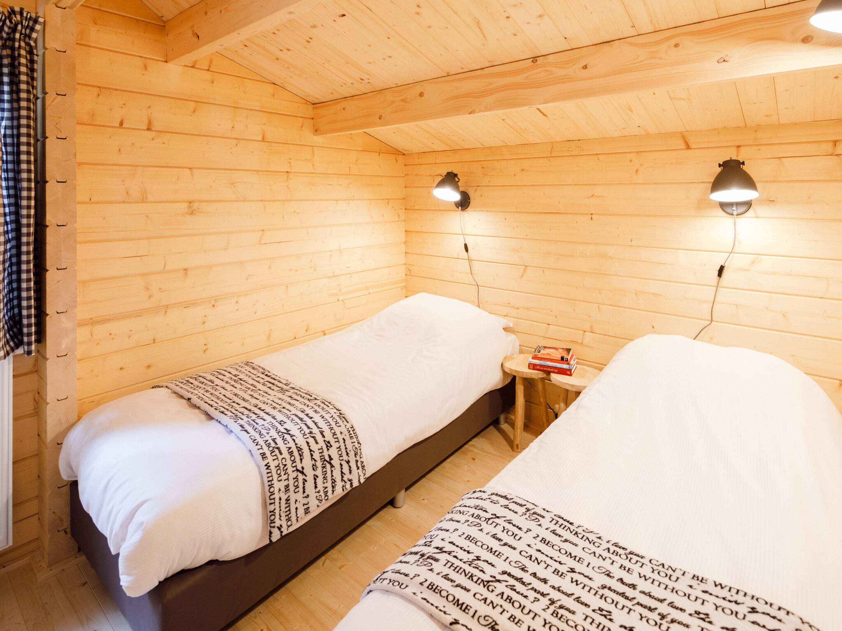 A cozy cabin room with two beds, wooden walls, and two wall-mounted lamps.