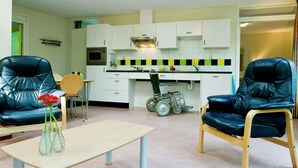 A modern kitchen with white cabinets, a microwave, and a gas stove. There are two black leather chairs and a small wooden table with vases. - Holiday Park Escape in Drenthe (Dwingeloo)