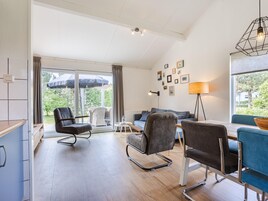 Una sala de estar moderna con un sofá, sillas, una mesa de comedor y vistas amplias a través de grandes ventanales.