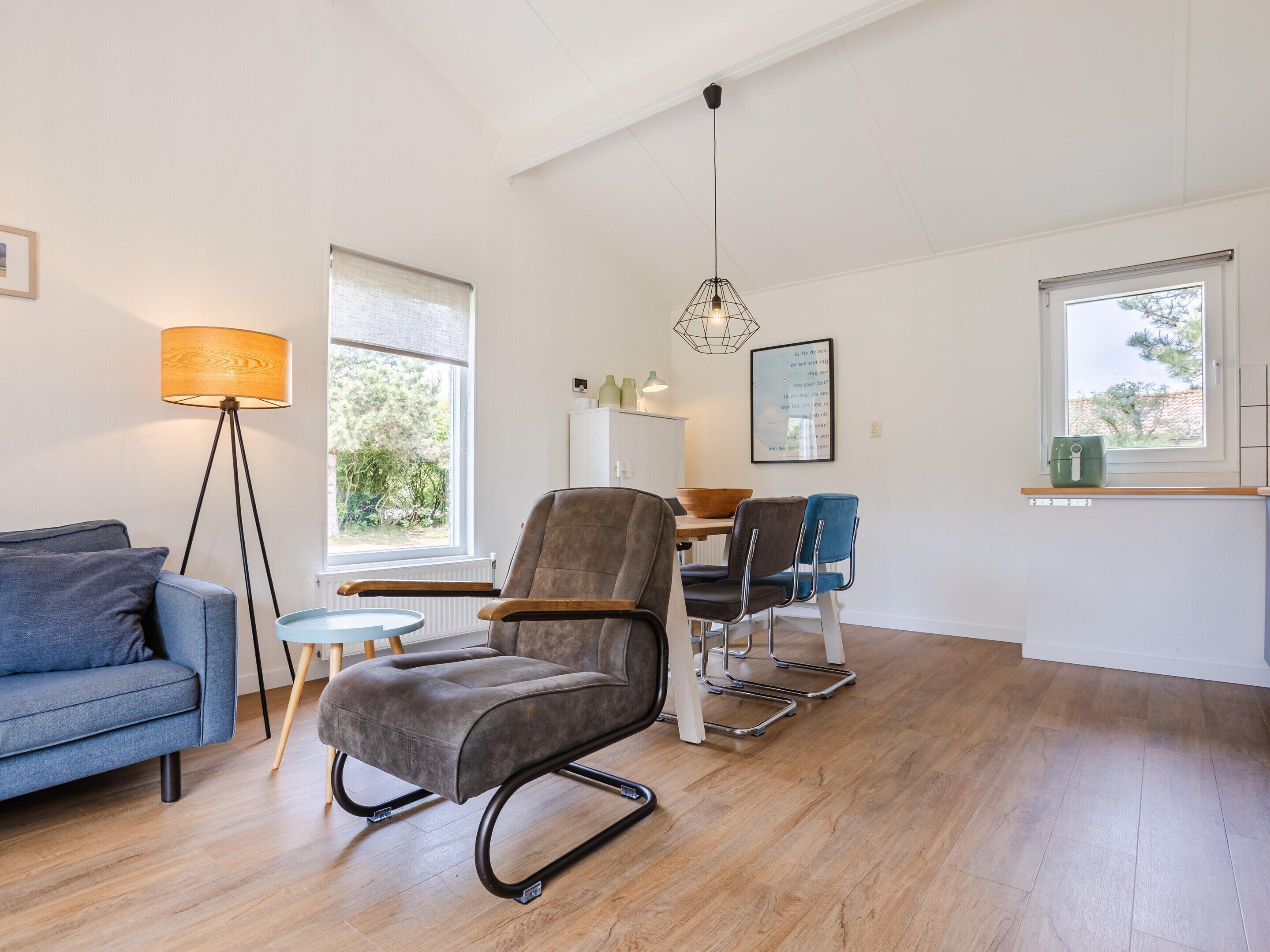 Un salon moderne comprenant un canapé, un fauteuil, une table à manger avec des chaises, une lampe sur pied et une suspension.