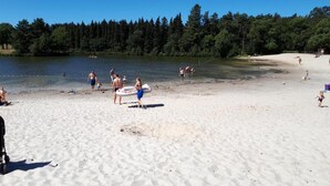 Ein Sandstrand mit Menschen, einem See und einem Wald im Hintergrund.