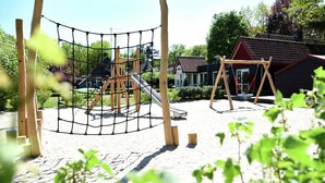 Ein Spielplatz mit einer Kletterkonstruktion mit Netz, einer Rutsche und einer Schaukel.