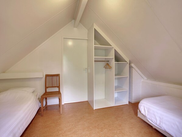 A bedroom with two beds, a wooden chair, a white wardrobe, and a sloped ceiling.