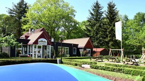 Ein Spielplatz mit einer blauen Rutsche, einem Gebäude mit rotem Dach, auf dem 'Gerner' steht, und einer Fahnenstange.