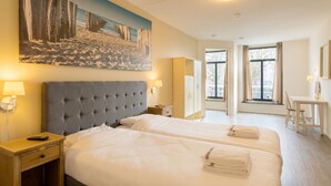 A hotel room with two beds, a painting of a beach scene, a desk, and a chair.
