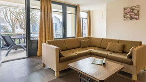 A living room with a sectional sofa, a wooden coffee table, and a view of the outside through large windows.